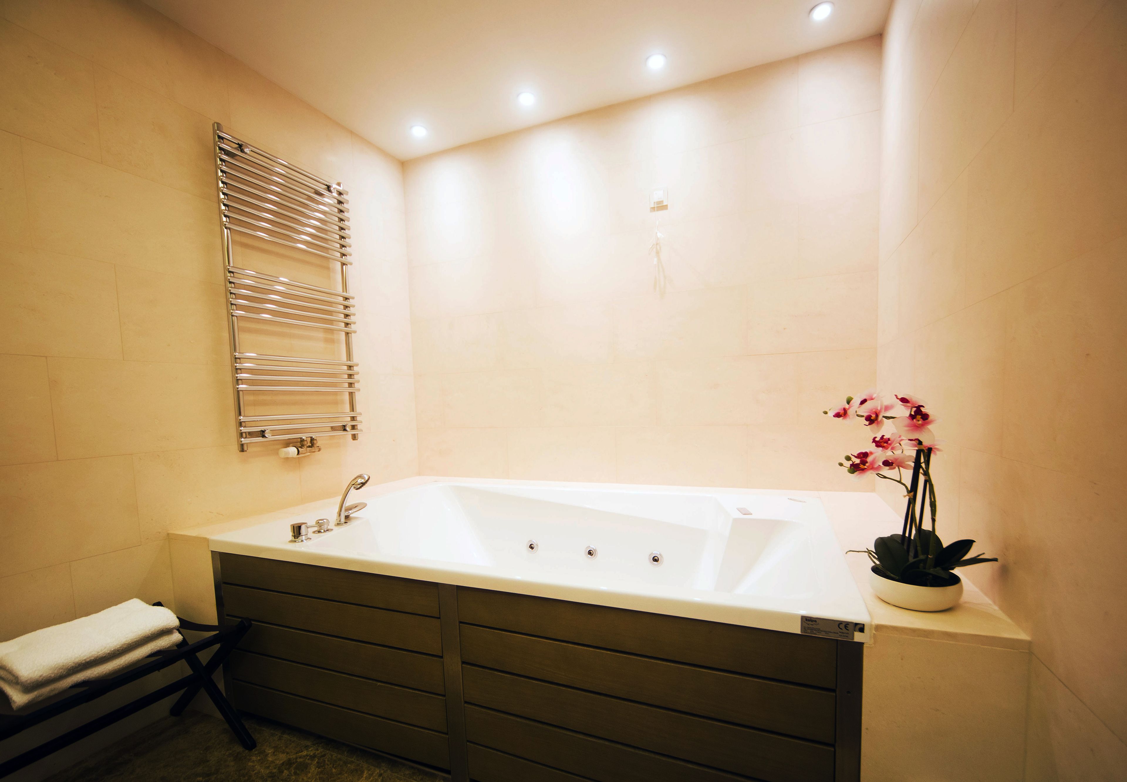 A modern bathroom with a large bathtub, a towel rack, and a potted orchid.