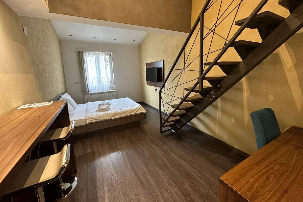 A compact room with a bed, a desk, and a staircase.