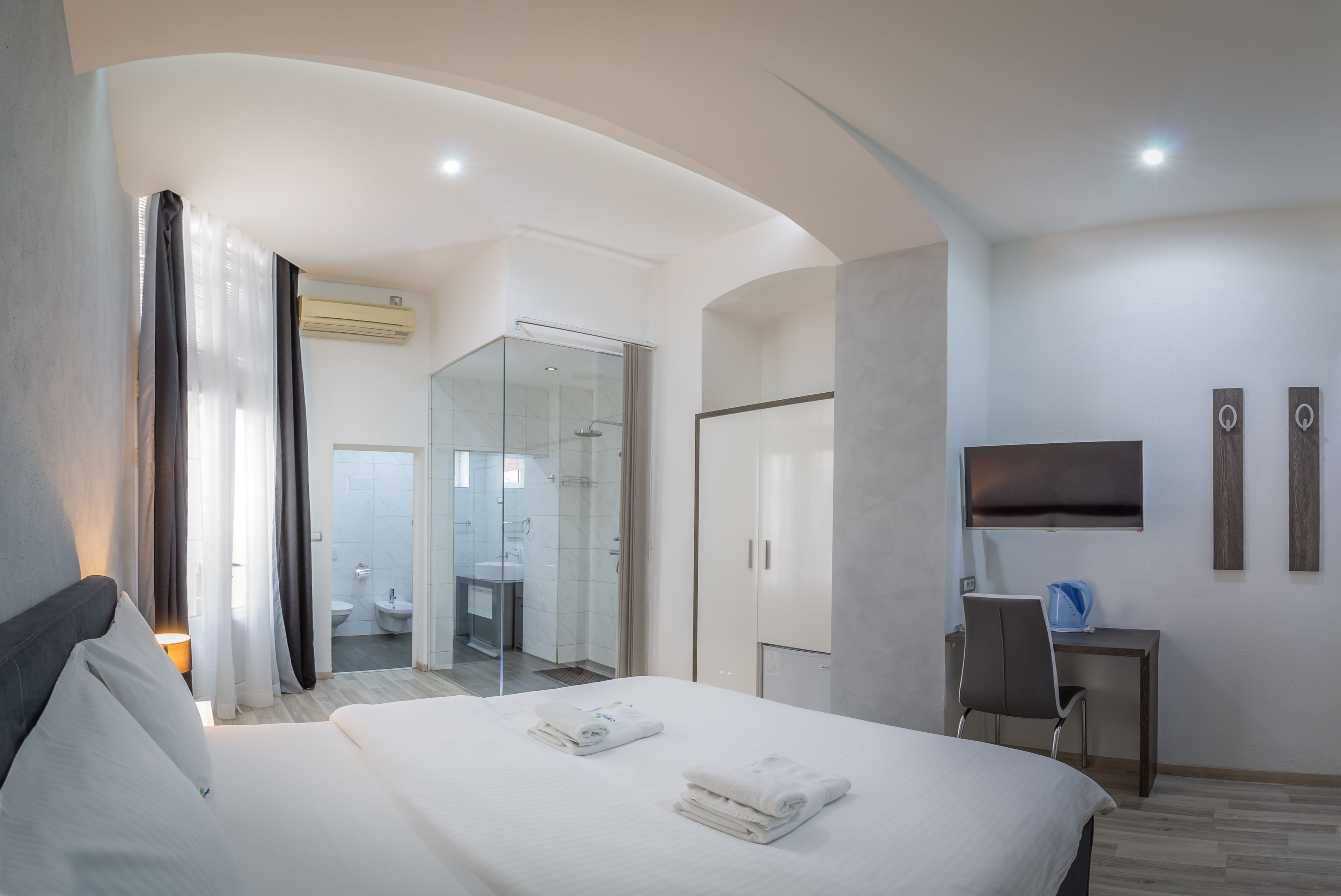 A modern hotel room with a large bed, a desk, a TV, and a bathroom visible through an open door.