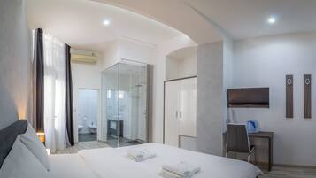 A modern hotel room with a large bed, a desk, a TV, and a bathroom visible through an open door.