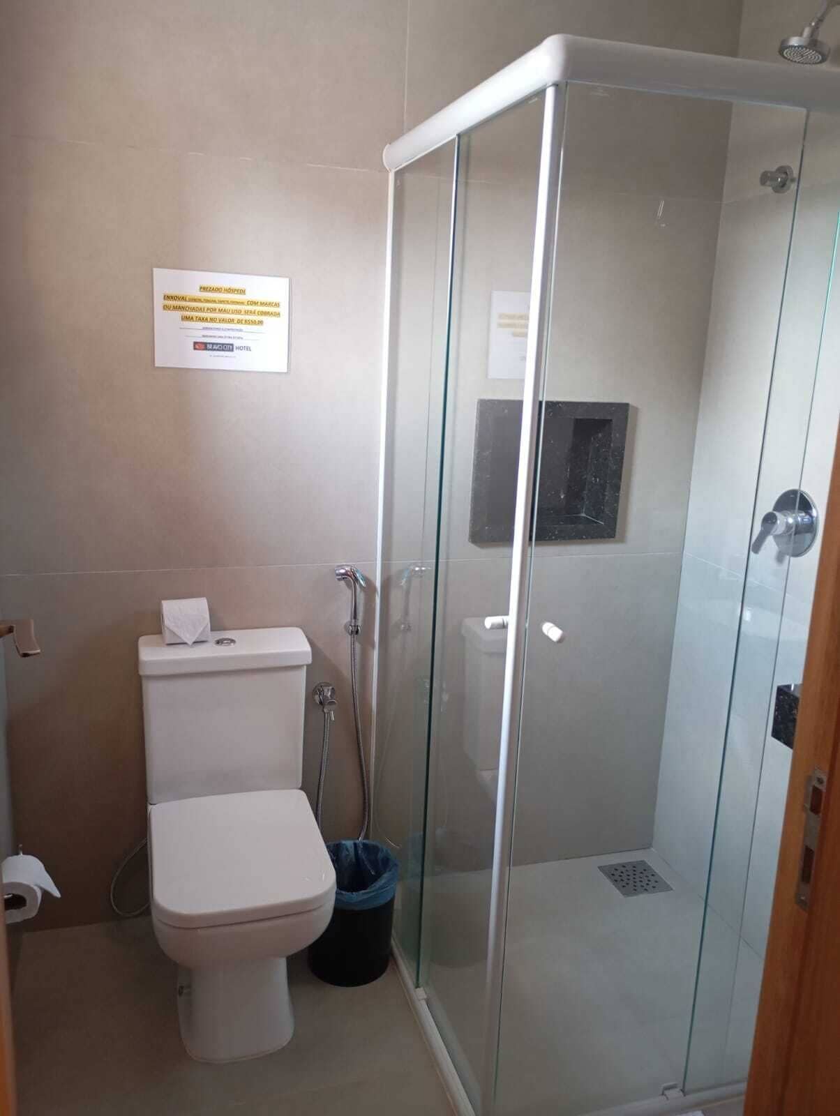 A bathroom with a glass-enclosed shower, a toilet, and a trash bin.