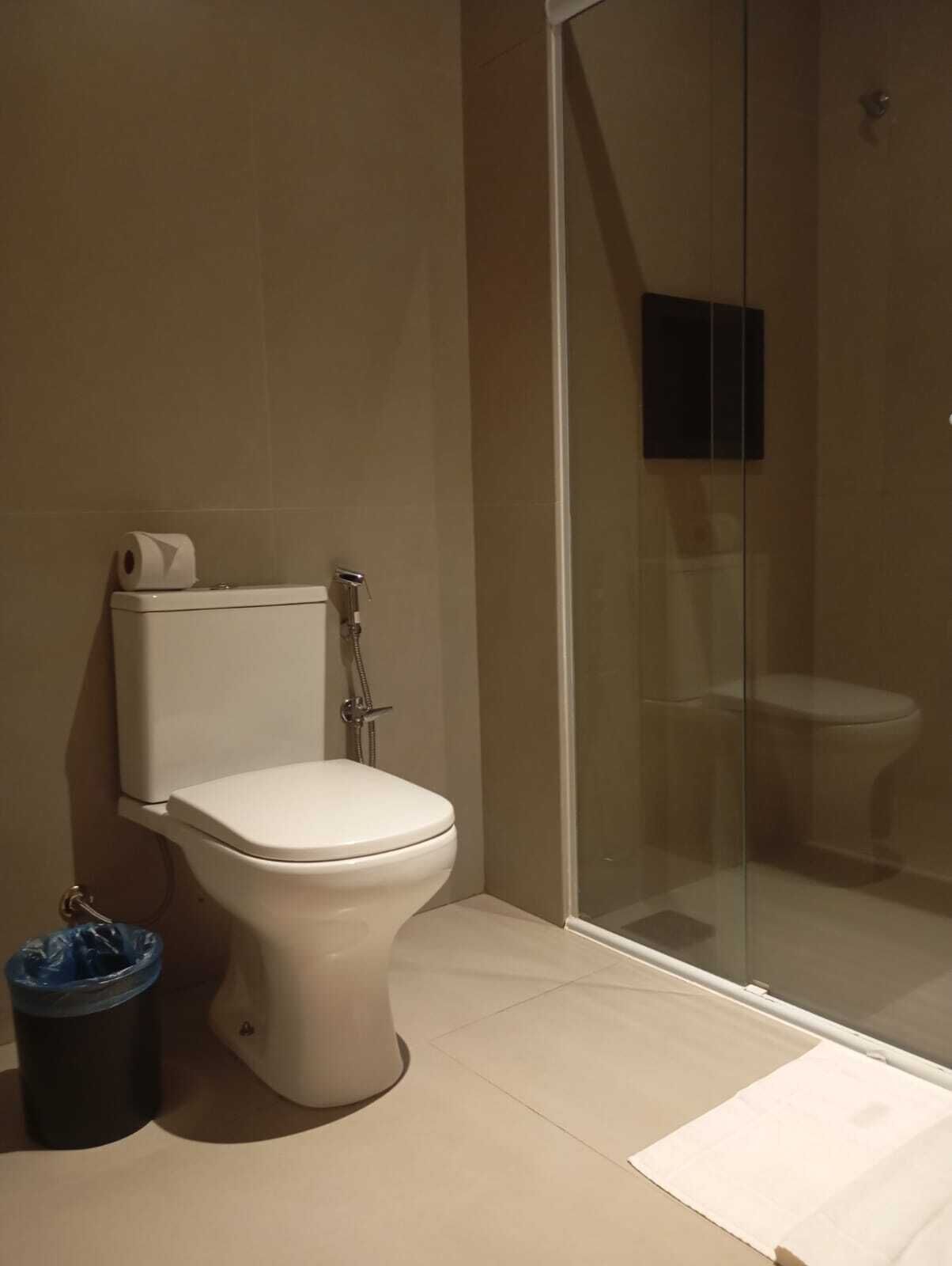 Un baño con inodoro, ducha con mampara de vidrio y un cubo de basura.
