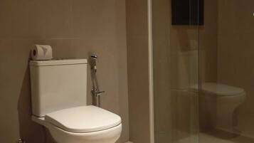 Un baño con inodoro, ducha con mampara de vidrio y un cubo de basura.