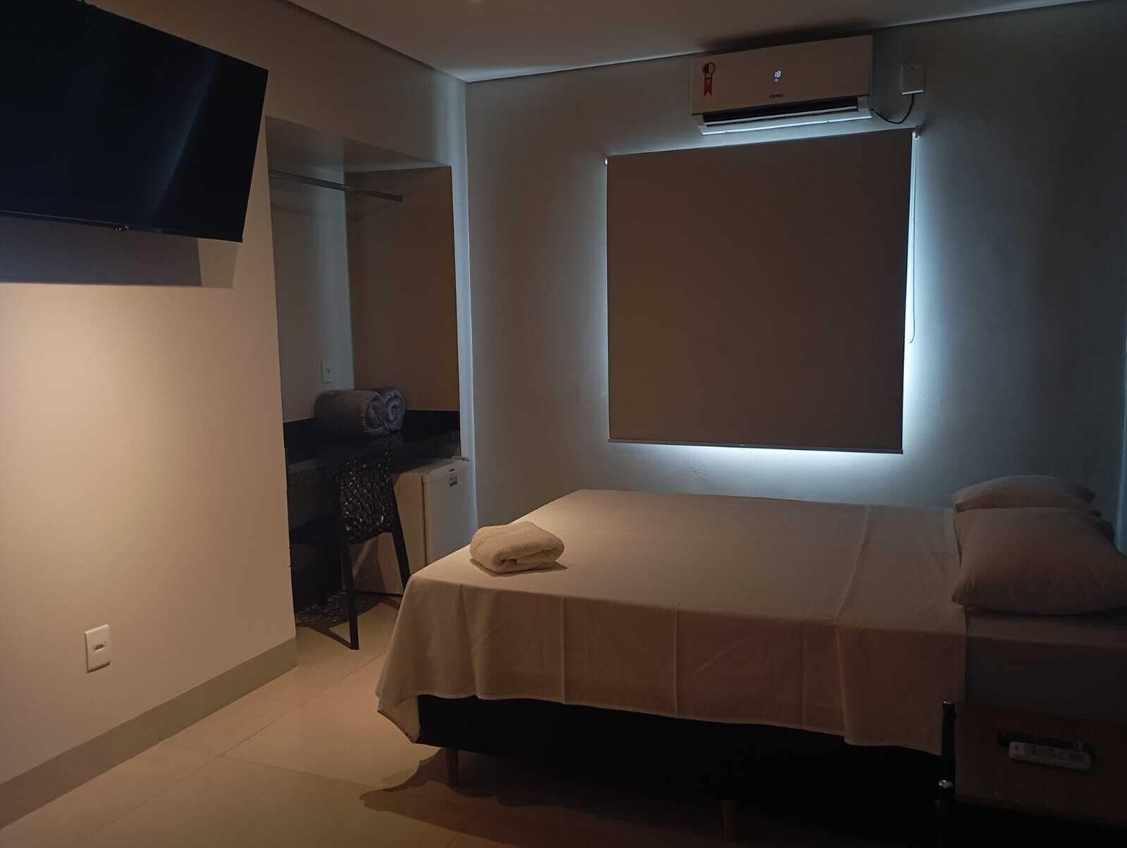 A small bedroom with a single bed, a desk, a chair, and a television mounted on the wall.