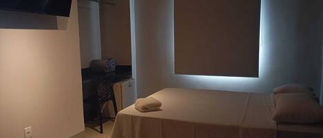 Una camera piccola con un letto singolo, una scrivania, una sedia e una televisione a parete.