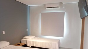 A hotel room with two beds, a flat-screen TV, an air conditioning unit, and a window. - Bravo City Hotel Dourados (Dourados)