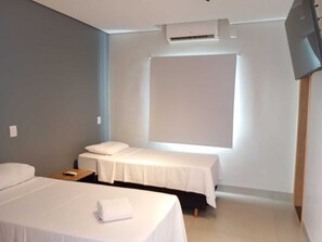 A hotel room with two beds, a flat-screen TV, an air conditioning unit, and a window. - Bravo City Hotel Dourados (Dourados)