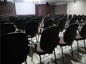 A conference room with rows of chairs facing a white projection screen. - Bravo City Hotel Dourados (Dourados)