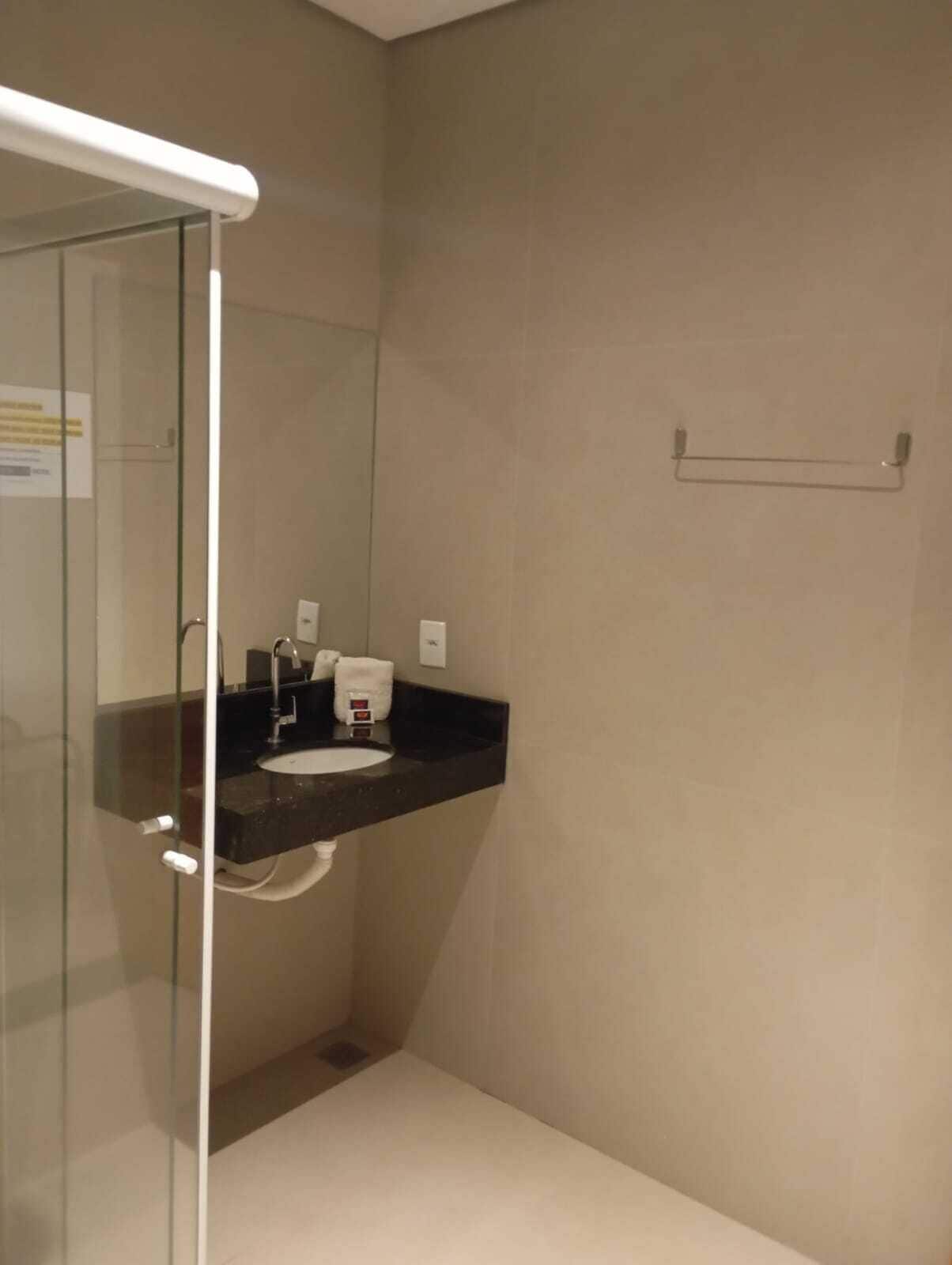 Un baño moderno con cabina de ducha de vidrio, lavamanos con encimera negra y un perchero para toallas.