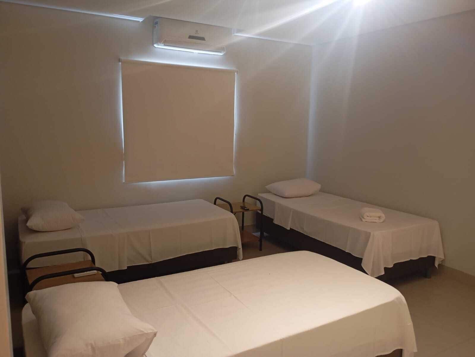 A room with two single beds, a chair, a window, and an air conditioning unit.