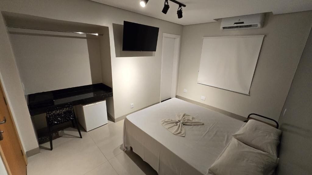Quarto com cama, escrivaninha, televisão e ar condicionado.