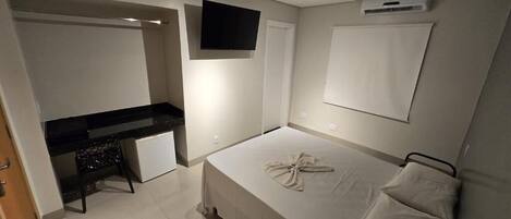 A bedroom with a bed, a desk, a television, and an air conditioning unit.