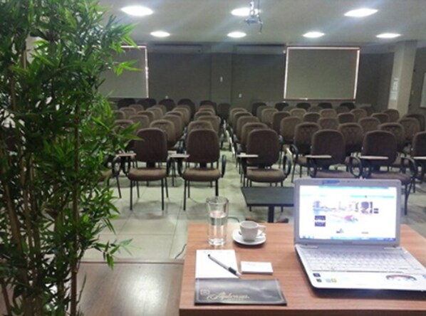 A conference room with rows of chairs, a laptop, a glass of water, and a notebook on a table. - Bravo City Hotel Dourados (Dourados)
