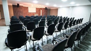 A conference room with rows of black chairs, a wooden panel wall, and a projector screen. - Bravo City Hotel Dourados (Dourados)