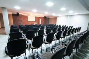 A conference room with rows of black chairs, a wooden panel wall, and a projector screen. - Bravo City Hotel Dourados (Dourados)