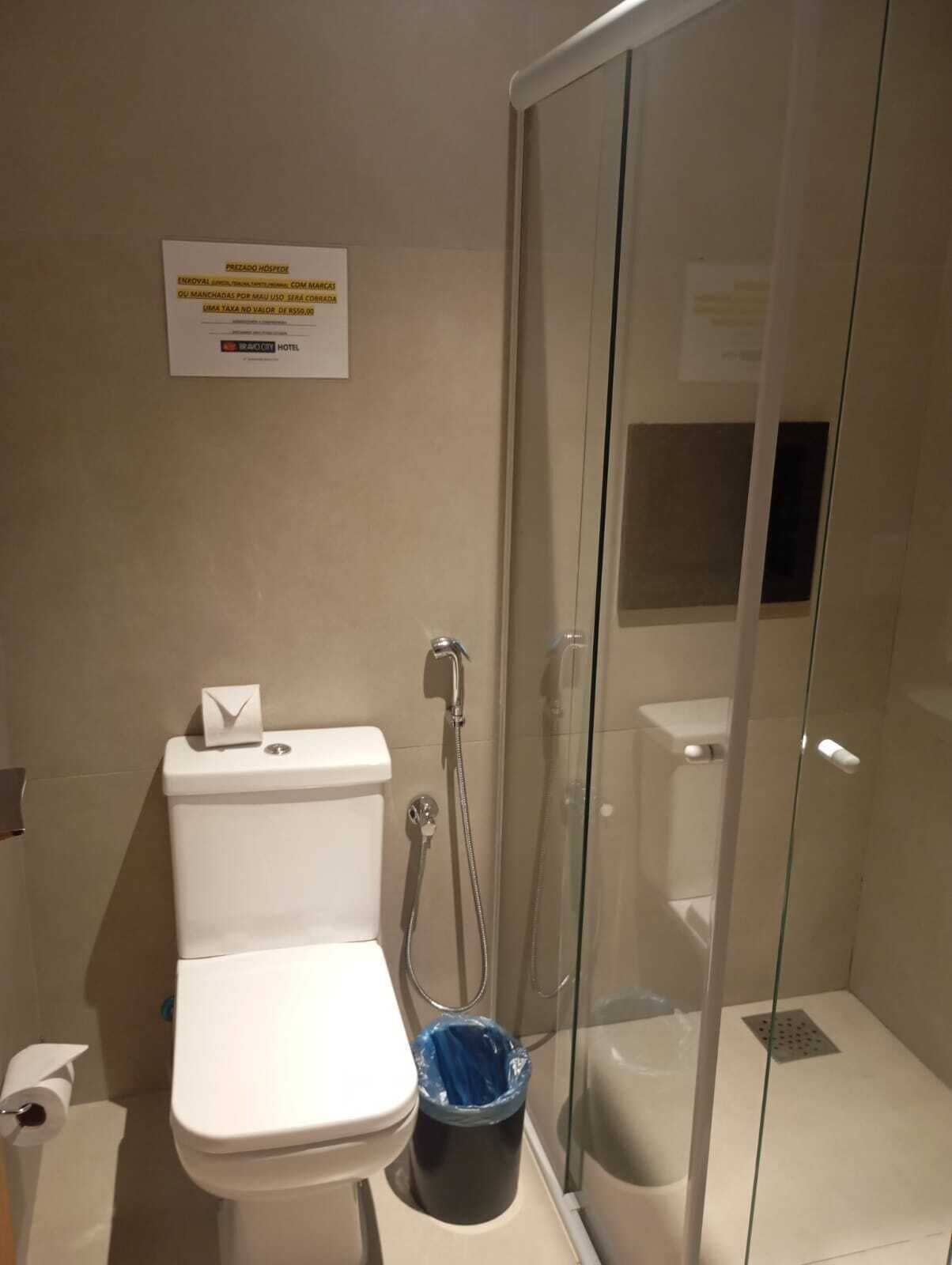 Un baño con inodoro, ducha con mampara de vidrio y un cubo de basura.