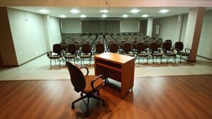 A conference room with rows of chairs, a wooden desk, and a projector screen. - Bravo City Hotel Dourados (Dourados)