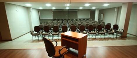 A conference room with rows of chairs, a wooden desk, and a projector screen.
