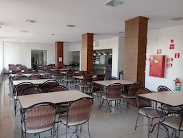 Un comedor amplio con varias mesas y sillas, una cocina al fondo y un extintor de incendios en la pared.