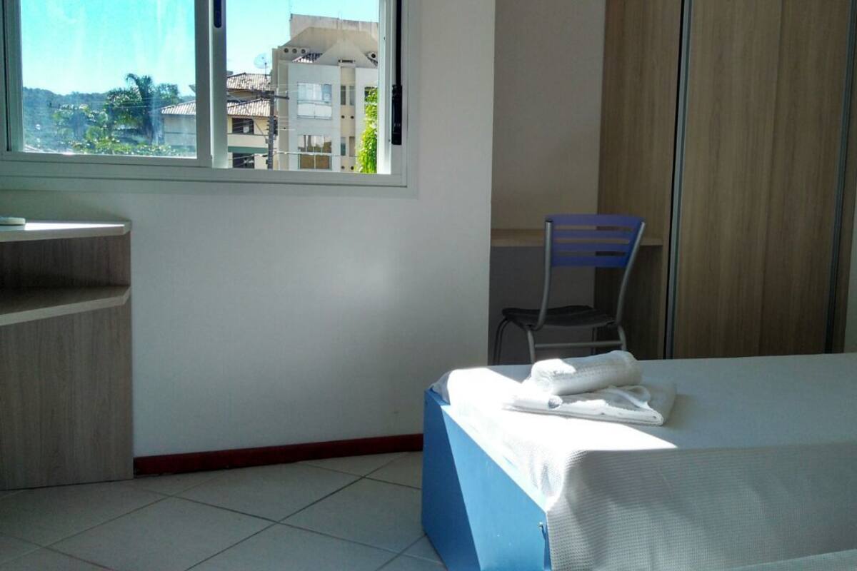 A hotel room with a bed, a desk, a chair, and a window with a view of buildings.