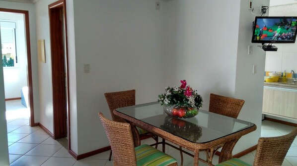 A dining area with a glass-top table, wicker chairs, and a floral centerpiece. - Brava Apart Hotel (Florianópolis)