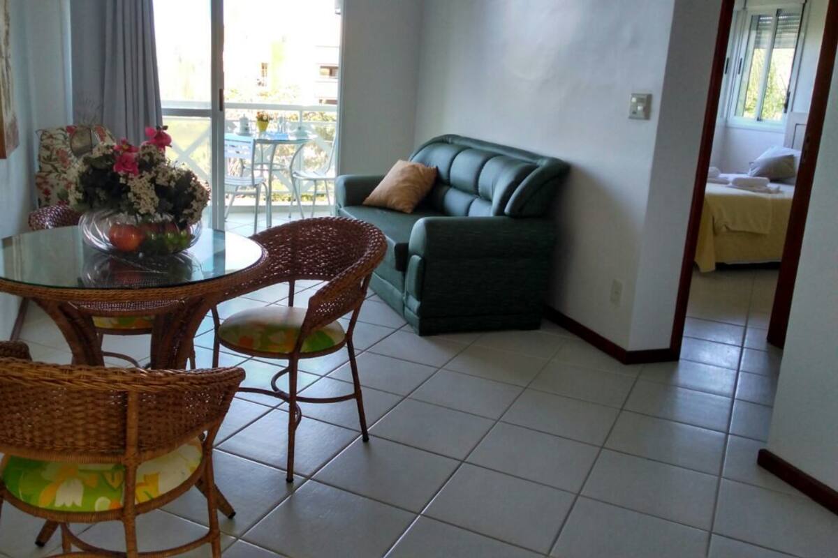 A dining area with wicker chairs, a glass table, and a vase with flowers. There is a green sofa in the background.