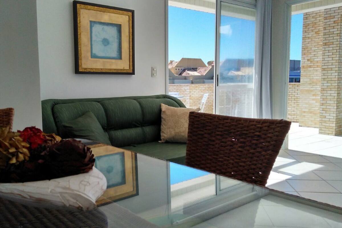 A modern living room with a glass coffee table, a green sofa with cushions, a wicker chair, and a framed picture on the wall.