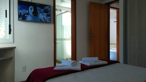 A hotel room with a bed, a TV mounted on the wall, and a door leading to a bathroom. - Brava Apart Hotel (Florianópolis)