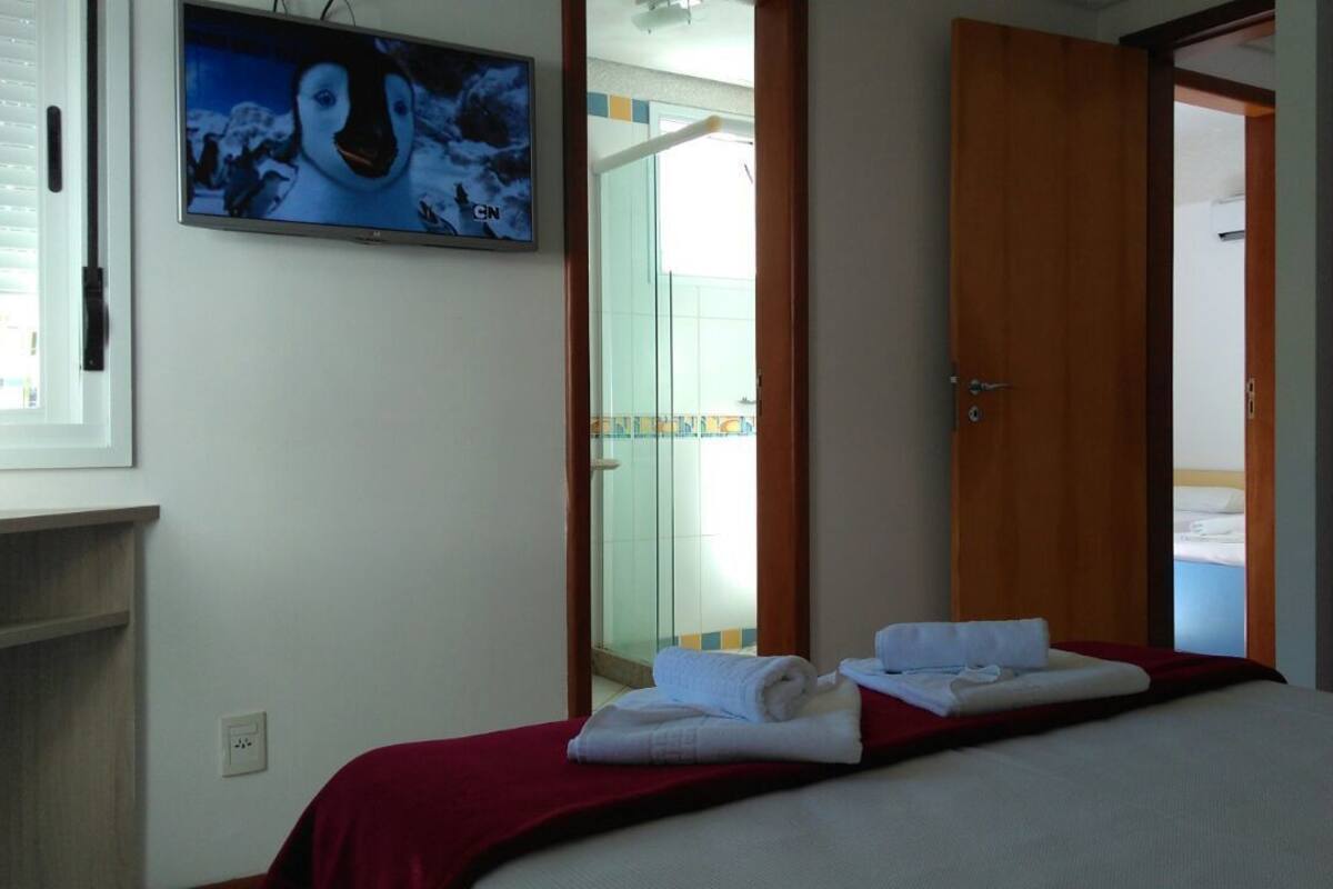 A hotel room with a bed, a TV mounted on the wall, and a door leading to a bathroom.