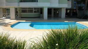 A swimming pool surrounded by a building with a flat roof and large windows. - Brava Apart Hotel (Florianópolis)
