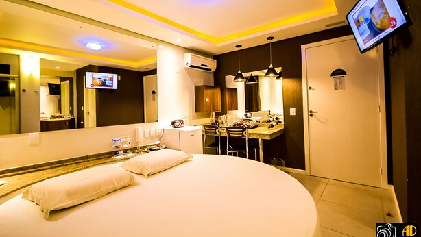 A hotel room with a large bed, a desk with a computer, a mirror, and a TV on the wall.
