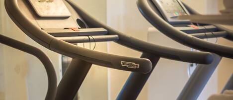 A treadmill with a digital display, a mirror, and a wall-mounted shelf.