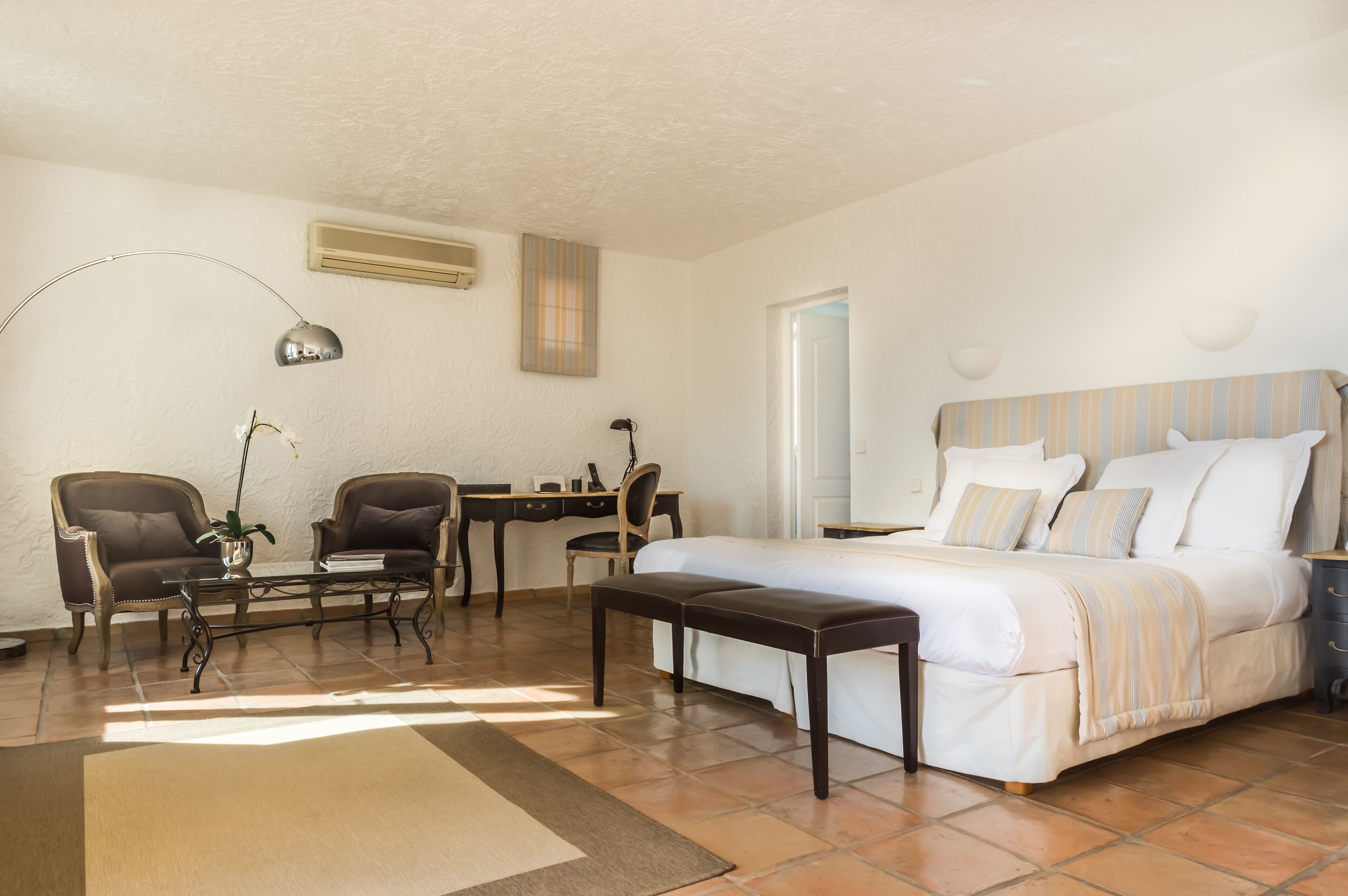 A hotel room with a bed, two armchairs, a desk, a lamp, and a small table.