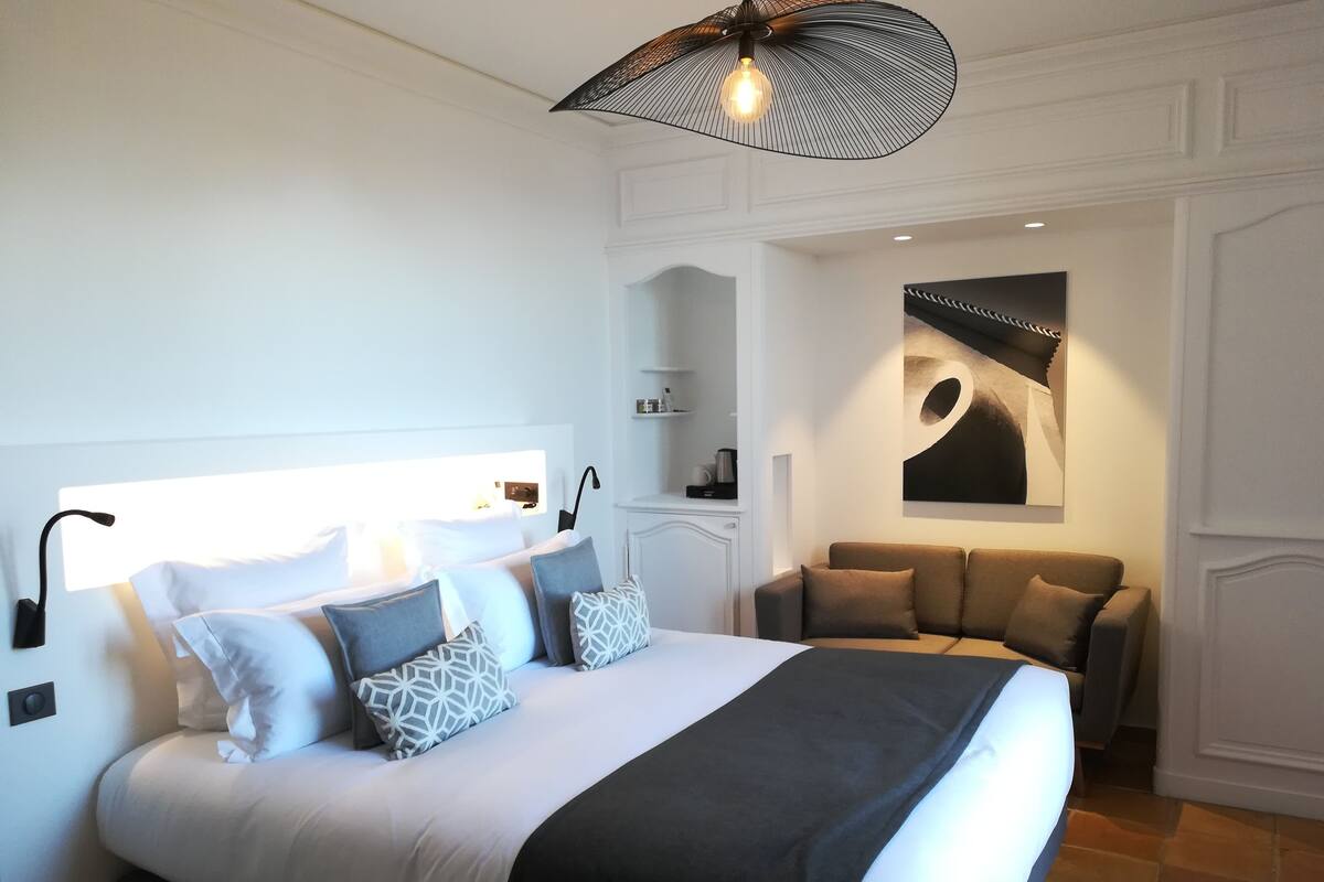 Ein modernes Schlafzimmer mit einem großen Bett, einer Couch, einer Wandleuchte und einer Deckenlampe.