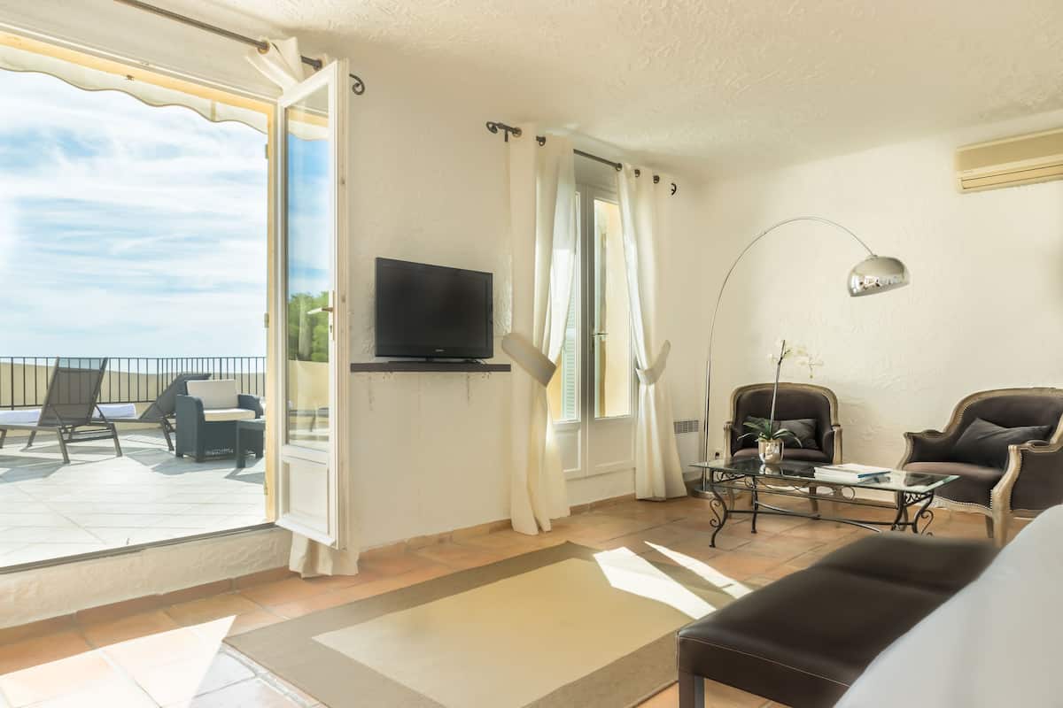 Ein Wohnzimmer mit Fernseher, zwei Sesseln, einem Couchtisch und Blick ins Freie.