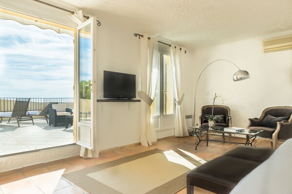 A living room with a TV, two armchairs, a coffee table, and a view of the outdoors. - Hôtel Club Port La Galère (Theoule-sur-Mer)