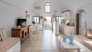 Un salón amplio con televisor, sofá y zona de comedor. Se observa una cocina con armarios y ventana.
