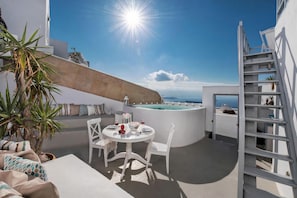 A sunlit outdoor dining area with a pool, white furniture, and a clear view of the sea. - Saint George Exclusive (Santorini)