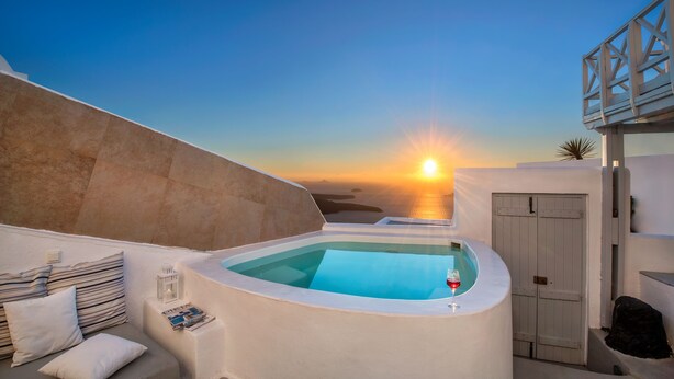 Una terraza en la azotea con piscina, una puerta y vistas a la puesta de sol sobre el mar.