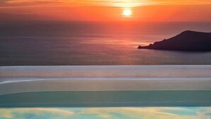 Atardecer sobre el océano con la silueta de una montaña y una playa en primer plano.