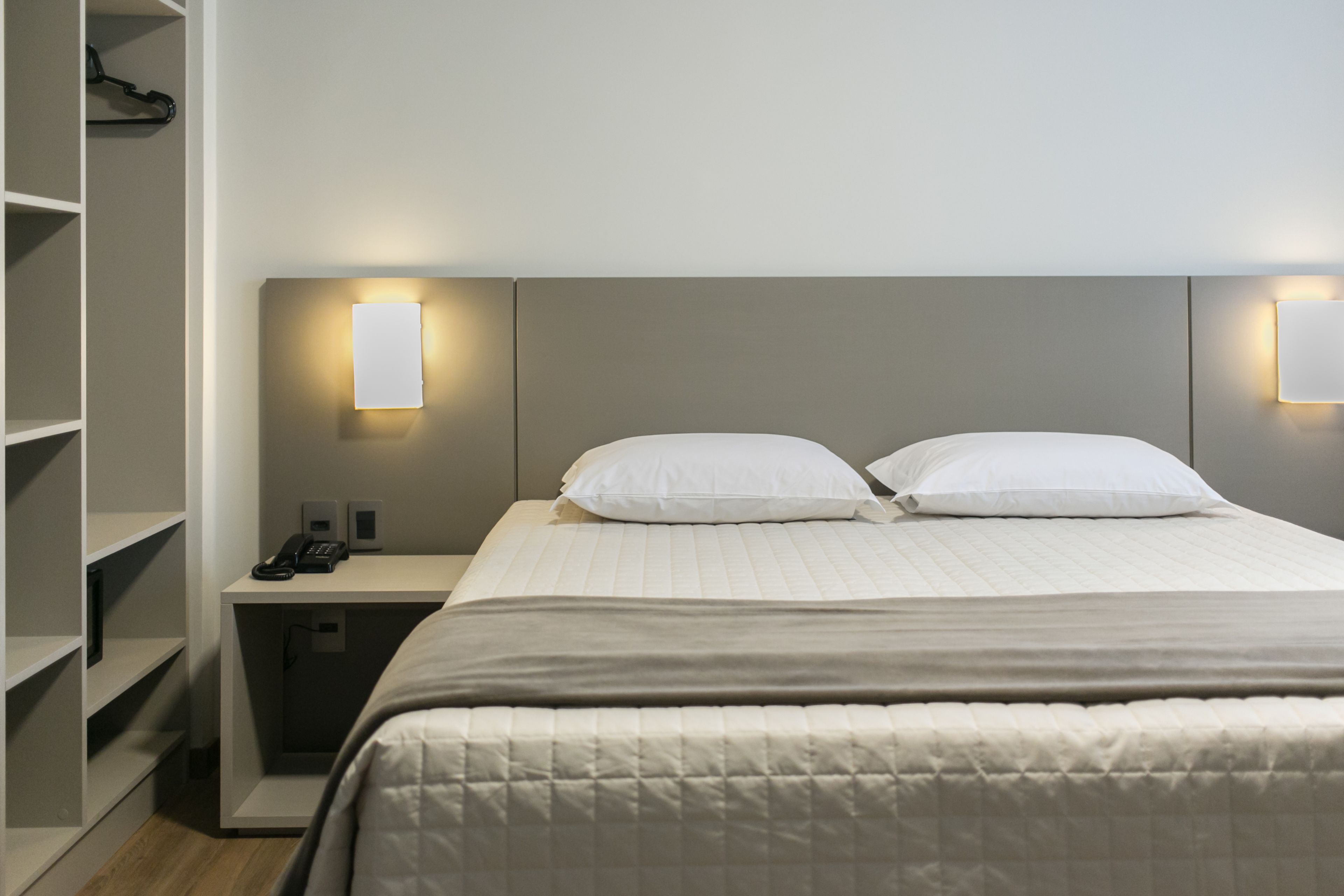Una habitación de hotel con cama, mesitas de noche, teléfono y lámparas fijadas a la pared.