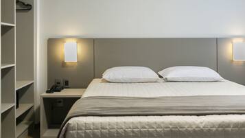 Una habitación de hotel con cama, mesitas de noche, teléfono y lámparas fijadas a la pared.