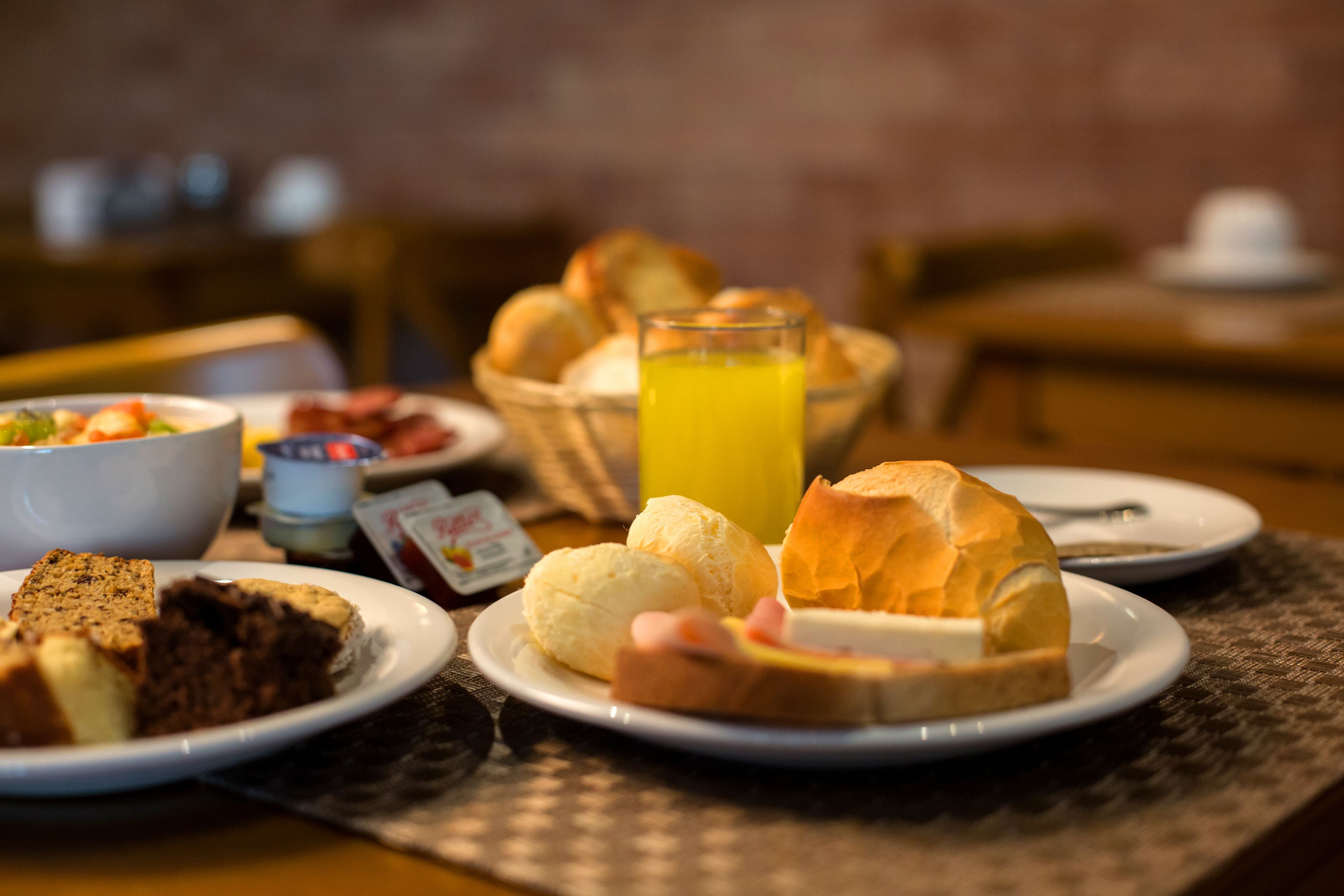 A breakfast setting with plates of food, a glass of orange juice, and a basket of bread.