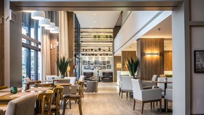 A spacious lobby with a high ceiling, modern lighting, and a mix of seating areas including a dining table and chairs. - Tri Hotel Premium Criciuma (Criciuma)