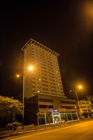 Un edificio de gran altura con varios pisos, una entrada visible y un área de estacionamiento al frente.