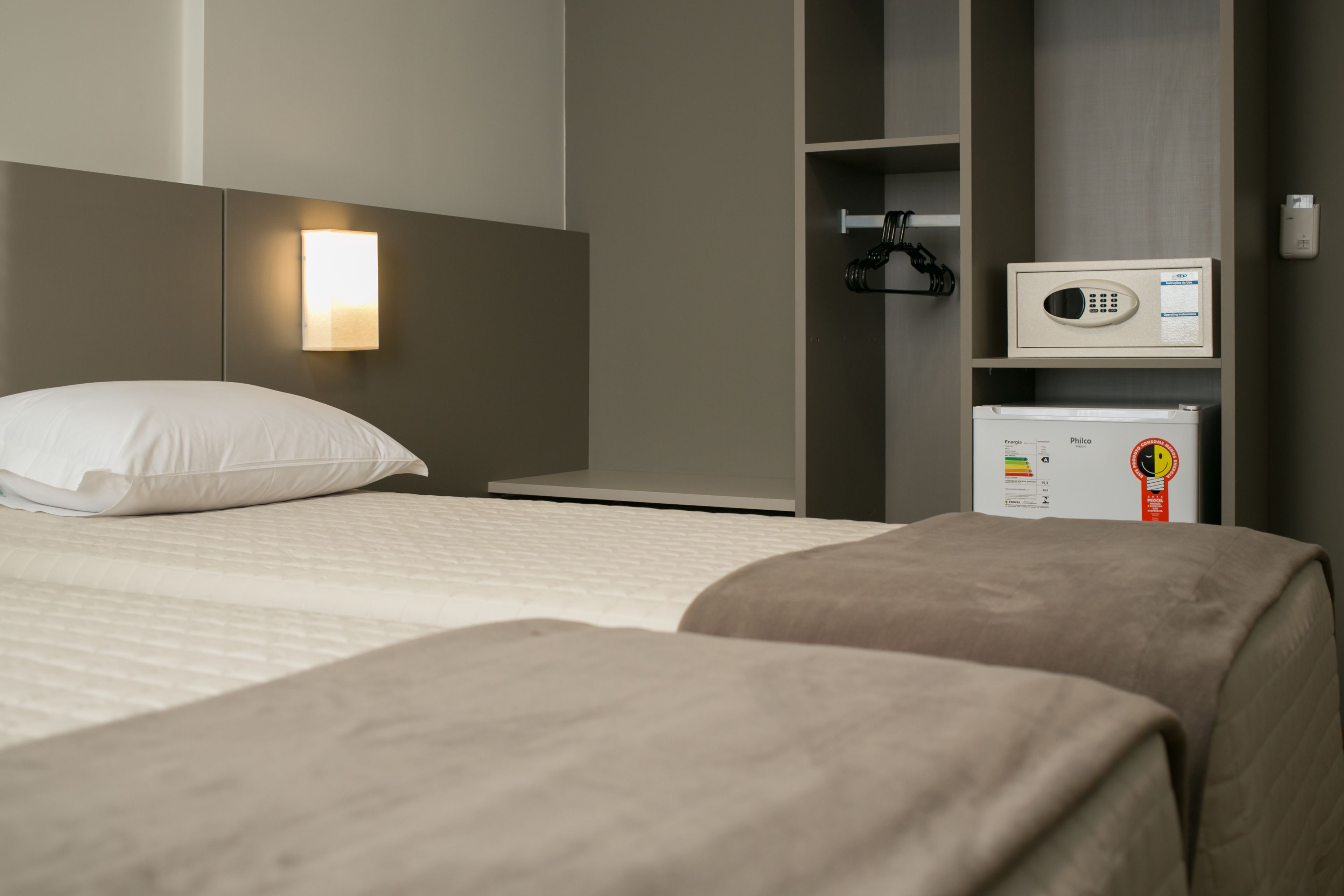 A hotel room with a bed, a bedside table, a wardrobe, and a minibar.