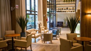 A modern lobby with seating areas, a reception desk, and a view of the street. - Tri Hotel Premium Criciuma (Criciuma)