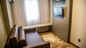 Una sala moderna con un sofá de cuero marrón, un televisor de pantalla plana montado, una ventana con cortinas translúcidas y un banco empotrado.