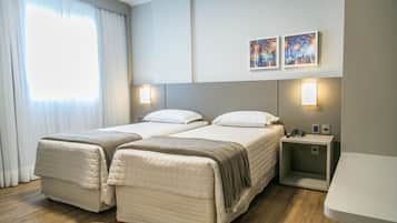 A hotel room with two beds, a nightstand, and two wall-mounted lamps.