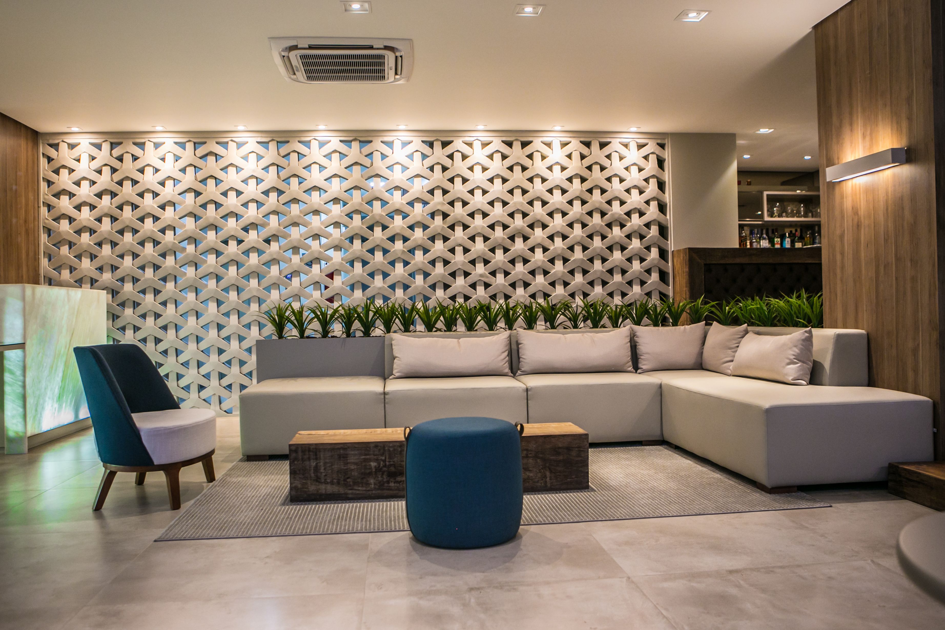 A modern living area with a sectional sofa, a blue ottoman, and a decorative wall with a geometric pattern.